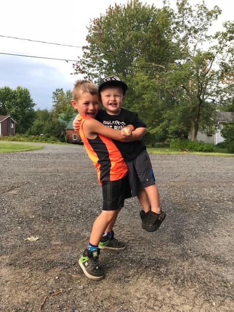 Rafaël laughing as his big brother Maksim hugs him and lifts him clean off the gravel driveway.