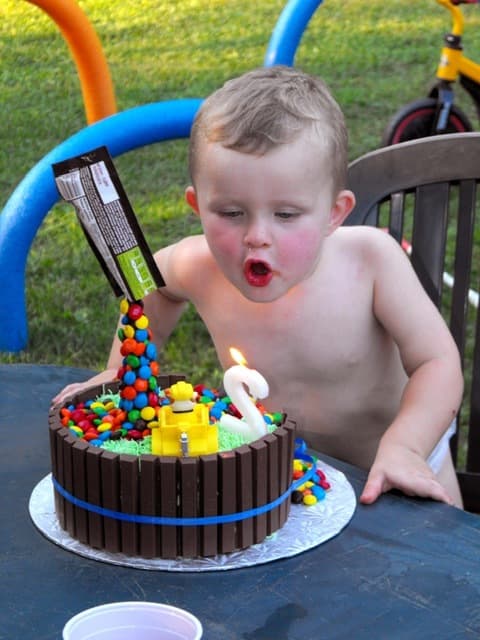 Rafaël leaning over his birthday cake, cheeks out, blowing at the number-two candle.